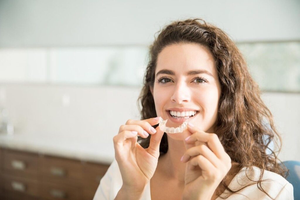 Patient holding a clear aligner tray and smiling during a consultation about How Long Does Aligner Treatment Take.