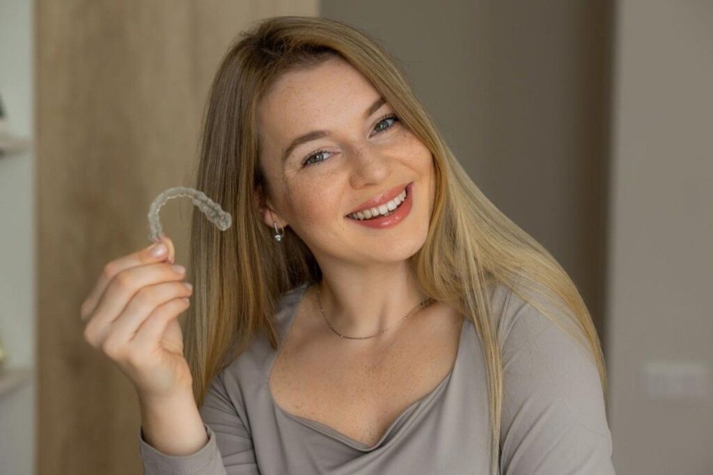 Patient smiling while holding clear aligner tray, illustrating the treatment process for invisible aligners.