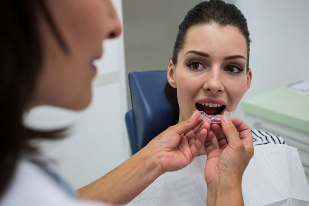 Treatment Process for Invisible Aligners showing a dentist placing a custom clear aligner tray during a professional orthodontic fitting appointment